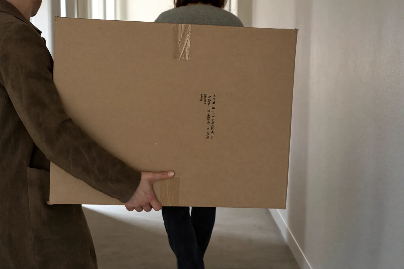 Zwei Personen tragen einen Karton: Eine Wohnung finden nach der Trennung heißt, unter Druck zu entscheiden